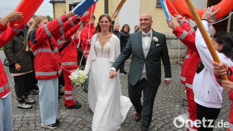 Freudestrahlend verlassen Simone und Sebastian Hecht die Plößberger Pfarrkirche und durchschreiten ein Ehrenspalier der Wasserwacht Weiden. Bild: kro