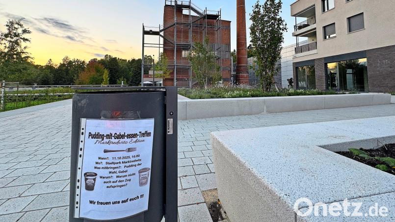 An einem Müllkübel im Auenpark hängt ein Plakat, das dazu einlädt, am 11. Oktober mitzumachen, wenn möglichst viele versuchen sollen, im Stadtpark mit einer Gabel Pudding zu essen. Bild: Matthias Bäumler