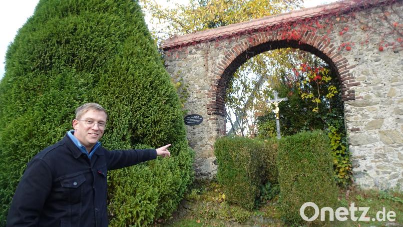 Tobias Knauer weist auf den Grabstein des Kirchenmalers Thaddäus Rabusky, der unter dem Eingangstor des ehemaligen fürstlichen Gartens in Neustadt/WN steht. Die zu wuchtig gewordene Zypresse hinter Knauer kommt weg. Bild: ui