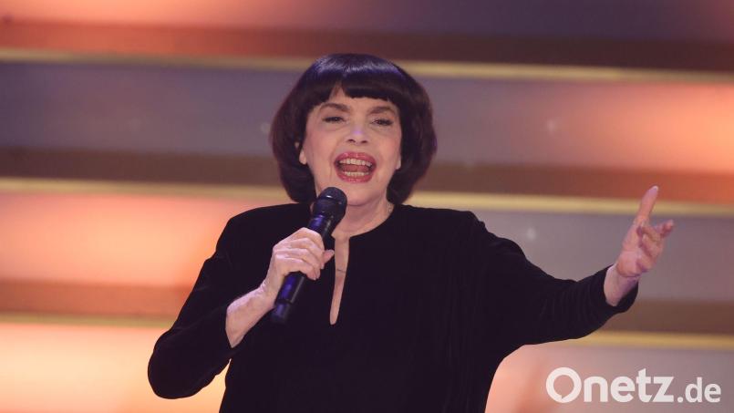 Mit Chanel-Hut und chinesischem Sonnenschirm schützt Chanson-Legende Mireille Mathieu ihre Haut. (Archivbild) Bild: Bodo Schackow/dpa