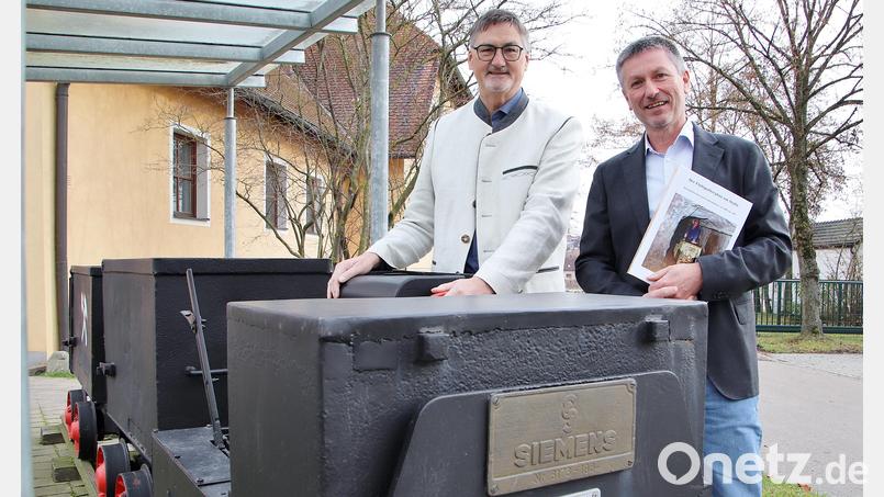 Autor Michael Ernstberger (rechts) mit seinem neuen Buch und der Stullner Bürgermeister Hans Prechtl bei der Siemens-Grubenlok, die vor dem Feuerwehrhaus in Stulln an die Zeit des Flusspat-Bergbaus in der Region erinnert. Bild: Thomas Dobler