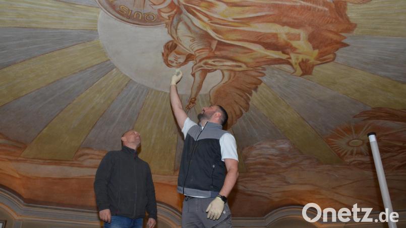 Diplom-Restaurator Enrico Ferretti (rechts) wischt fast zärtlich über das Gesicht des Erzengels Michael, der in majestätischer Größe im Zentrum der Kuppel in der katholischen Stadtpfarrkirche schwebt. Kirchenmaler- und Vergoldermeister Martin Eis begutachtet das Werk. Bild: dob