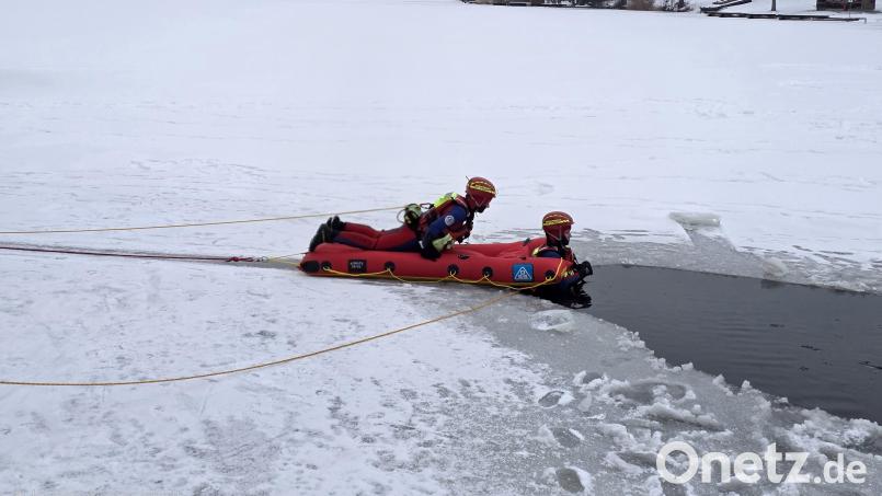 Ein Wasserretter kommt mit einem Eisrettungsschlitten einer im Eis eingebrochenen Person zu Hilfe. Der Schlitten und der Wasserretter sind durch ein Seil gesichert. Während der Übung auf dem Rußweiher in Eschenbach war auch die eingebrochene Person vom Ufer aus durch ein Seil abgesichert. Bild: Josef Ott