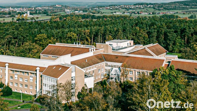 Zwischen Bäumen eingebettet liegt die Asklepios-Klinik Lindenlohe bei Schwandorf, die sich auf orthopädische Behandlungen spezialisiert hat. Sie existiert seit 75 Jahren und ist seit zwei Jahrzehnten Teil der Asklepios-Gruppe. Im Hintergrund sieht man Schwarzenfeld (links) und die Kirche auf dem Miesberg. Bild: Asklepios-Klinik/exb