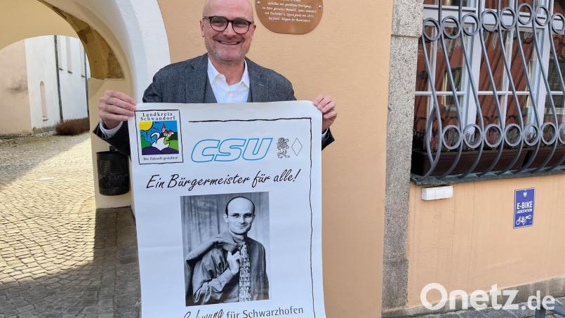 Maximilian Beer vor dem Rathaus in Schwarzhofen, in dem er sechs weitere Jahre der Chef ist. Er hat sein allererstes Wahlplakat von 1996 hervorgeholt. Das locker über der Schulter hängende Jackerl gefällt damals nicht jedem. Bild: ihl