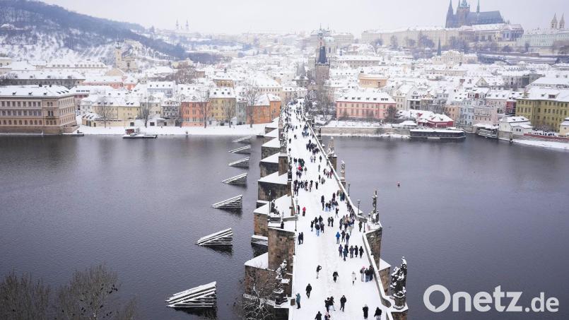 Menschen überqueren die mittelalterliche Karlsbrücke nach starkem Schneefall. Bild: Petr David Josek/AP/dpa