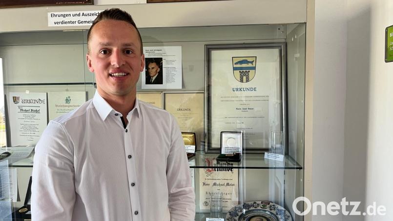 Der neue Bürgermeister von Schmidgaden, Martin Bauer, steht vor der Vitrine im Eingang zum Rathaus. Im Hintergrund ein Bild seines Urgroßvaters Josef Bauer. Er war ebenfalls Bürgermeister von Schmidgaden und ist Ehrenbürger. Martin Bauer heißt mit zweitem Vornamen Josef wie sein Urgroßvater. Bild: ihl