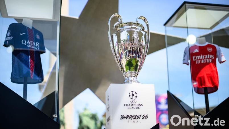 Der Pokal der Champions League steht zwischen den Trikots der Finalteams Paris Saint-Germain und FC Arsenal. Bild: Tom Weller/dpa