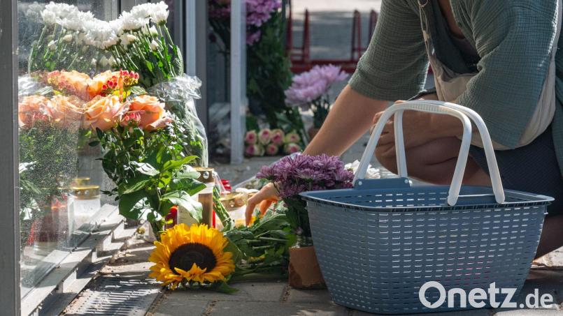 Eine Frau legt eine Karte zu Blumen und Kerzen, die vor der Bankfiliale abgelegt wurden. Nach der tödlichen Messerattacke in einer Regensburger Bank versucht die Kriminalpolizei weiter, die Hintergründe aufzuklären. Bild: Armin Weigel/dpa