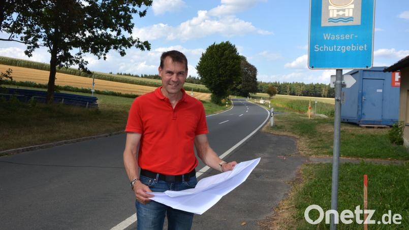 Bürgermeister Andreas Malzer mit den Plänen zur Wasserleitungserneuerung in Groppenheim, im Hintergrund die Kreisstraße TIR 15 in Richtung Münchenreuth, die ab Montag, 17. August, komplett gesperrt sein wird. Bild: Josef Rosner