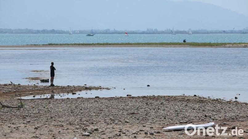 Es bleibt heiß in Bayern: Ein Mann steht am trockenen Ufer des Bodensees neben einem Surfboard. (Archivbild) Bild: Karl-Josef Hildenbrand/dpa