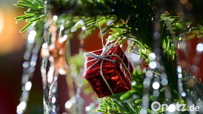 Ein kleines rotes Geschenkpaket als Weihnachtsbaumanhänger und Lametta hängen an einem Weihnachtsbaum. Bild: Jens Kalaene/dpa