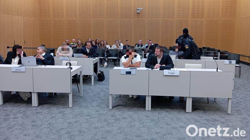 Der Angeklagte (hinten rechts) wird von vermummten Polizeibeamten in den Saal verbracht. Er soll zusammen mit einem 31-Jährigen (hinten links) aus dem Krankenhaus heraus mit Drogen gedealt haben. Die Mitangeklagte (vorne links) habe sich zusammen mit ihrem Fahrer (vorne rechts) "draußen" um die Geschäfte gekümmert. Bild: Kathrin Halbhuber