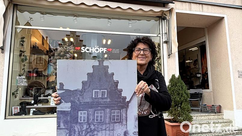 Ulrike Scherm vor ihrem Schuhfachgeschäft in Kemnath: Das historische Foto dokumentiert, wie es Mitte der 1920er-Jahre ausgesehen hatte, kurz bevor ihre Großeltern das Haus gekauft hatten. Bild: Holger Stiegler