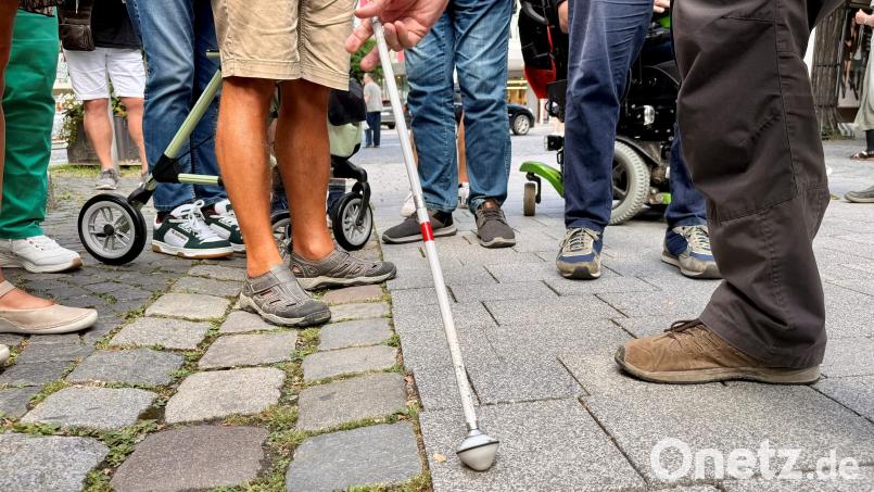Ein Mann fährt mit seinem Leitstock an der Kante zwischen Pflastersteinen und Granitplatten entlang. Sie dient hier als Leitlinie. Bild: Gabi Schönberger