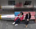 Zwei Frauen sitzen in Peking auf einer Bank, die mit der US-Flagge dekoriert ist. China will als Reaktion auf Strafzölle der USA mit Handelsstrafen gegen Washington antworten.	Bild: Ng Han Guan/dpa