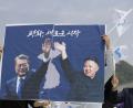 Südkoreaner halten ein Plakat, das Moon Jae In (links), Präsident von Südkorea, und Kim Jong Un, den Machthaber in Nordkorea, zeigt. 
 	Bild: Lee Jin-Man/dpa