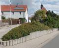 Bild: Brendel, Hubert (BR)
Die Betonpalisaden südlich der Sankt Anna Kirche (Mitte, im Hintergrund) sollen bei den Maßnahmen im Zuge der einfachen Dorferneuerung, vorbehaltlich einer Förderung, durch eine dorfgerechte Trockenmauer aus Granitsteinen ersetzt werden. Gleichzeitig soll das schadhafte Betonpflaster im Gehweg erneuert werden. Die dafür veranschlagten Kosten belaufen sich auf rund 54 000 Euro.