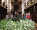 Bild: ubb
Mit vereinten Kräften und der Hilfe von Mesner Michael Burger und Kaplan John Gali haben die Frauen auch heuer wieder einen imposanten Adventskranz für die Basilika gebunden.