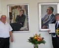 Bild: weu
Vor den Portraits des Ehepaars Max und Margret Schwarz, deren Vermächtnis im Arbeitsleben von Wolfgang Ruhland (rechts) eine tragende Rolle spielt, überreichte Bürgermeister Weigl die Urkunde zum Dienstjubiläum.