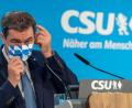 Bild: Peter Kneffel
Markus Söder (CSU) steht auf einem Podium und setzt sich seine Mundschutzmaske auf. Foto: Peter Kneffel/dpa