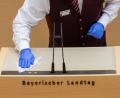 Bild:  Peter Kneffel/dpa
Ein Mitarbeiter des Landtags desinfiziert während der Plenarsitzung des bayerischen Landtags das Rednerpult.