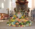 Bild: rpp
Der Erntegaben sind am historischen Taufstein der Dreieinigkeitskirche und auf einem Leiterwagen dekoriert. Im Hintergrund sind Stellwände mit Fotos zu sehen: „Vom Korn zum Brot“ – oder besser „Ein Brot erzählt aus seinem Leben“.