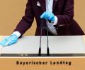 Bild: Sven Hoppe/dpa
: Eine Mitarbeiterin des Bayerischen Landtags desinfiziert das Rednerpult und die Mikrofone.