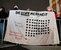 Symbolbild: Stringer/dpa
Teilnehmer einer Demonstration gegen die sogenannten „Spaziergänge“ (vorne), halten den vorbeilaufenden Teilnehmern eines Protestes gegen die aktuellen Coronamaßnahmen Banner wie „Die ECHTE Mehrheit“ entgegen.