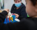 Symbolbild: Sebastian Gollnow/dpa
Ein Junge spielt in einer Kita. Im Hintergrund sitzt eine Erzieherin, die eine medizinische Maske trägt.