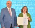 Bild: StmGP/exb
Peter Bauer (links), der Patienten- und Pflegebeauftragte der Bayerischen Staatsregierung, zeichnet Cornelia Lochner aus Amberg aus.