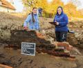 Bild: Hösamer, Clemens
Die Archäologinnen Ingrid Tamerl-Seiler (links) und Magdalena Haberl stehen an den Resten einer Ziegelmauer auf dem Grundstück Schloßstraße 17 in Schwarzenfeld. Am Boden links ist eine dunkle Schicht zu erkennen, die eventuell von einer Brandkatastrophe im 19. Jahrhundert stammt. Das Schild im Vordergrund hilft, die genaue Stelle später auf den Bildern der Archäologen zuzuordnen.