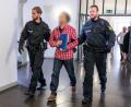 Bild: Armin Weigel
Der Angeklagte, der dreifach gefesselt ist, wird von Polizisten zum Gerichtssaal geführt.