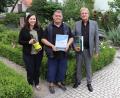 Bild: Stadt Tirschenreuth/exb
Dritter Bürgermeister Norbert Schuller (rechts) und die Leiterin der Tourist-Info, Birgit Plößner (links), überreichten Jörg Wolf zum Urlaubs-Jubiläum neben einer Urkunde auch die aktuelle Chronik der Stadt Tirschenreuth und eine Flasche Wein.