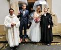 Bild: hzi
Das Brautpaar Vanessa und Christopher Schraml, eingerahmt von Pater Samuel Patton aus Creußen (links) und Pfarrerin Sabine Winkler aus Pegnitz (rechts), nach der Trauung am Kirchenportal der Heinersreuther Waldkapelle.