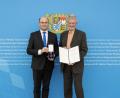Bild: StMFH/Christian Blaschka/exb
Finanz- und Heimatminister Albert Füracker (links) überreicht das Bundesverdienstkreuz am Bande an Georg Pillhofer.