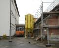 Bild: bey
Zwischen der Schule (links) und der Mehrzweckhalle (rechts) muss das Stahlrohr für die Aufnahme von Kanal und Wasserleitung verlegt werden. Es ist ein echter neuralgischer Punkt, weil das Stahlrohr tiefer gelegt werden muss als die Fundamente der beiden Gebäude in den Boden verbaut sind. Außerdem ist das Grundwasser ein nicht zu übersehendes Problem.