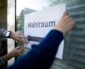 Bild: Fabian Strauch/dpa
Wahlhelfer hängen einen Zettel, auf dem „Wahlraum“ steht, auf.