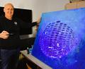 Bild: ubb
Jürgen Frischholz zeigt als Beispiel eines der fluoreszierenden Gemälde, das er selbst gemalt hat. Das Bild gibt es auch bei der Ausstellung zu sehen. Bei entsprechend richtiger Leuchttechnik wird der Effekt natürlich weit eindrucksvoller herausgearbeitet sein.