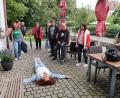 Bild: bsc
Zur Freude der Teilnehmer wurden bei der Drehort-Tour durch Friedenfels auch Szenen nachgespielt, wie hier von Ulla Britta Baumer (auf dem Boden liegend) die Szenerie, als sie im Film mausetot vor der Eingangstür des Friedenfelser Dorfladens liegen musste.