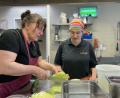 Bild: Paulina Schmidt
Vormittags bereiten die Mitarbeitenden alle Zutaten vor, die sie für kleine Beilagensalate brauchen. Uschi (links) zeigt Anna, wie sie den Salat dafür schneiden soll.
