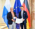 Bild: Joerg Koch/Bayerische Staatskanzlei
Wilhelm Koch (links) hatte sich für die Ehrung in München extra sein Europa-Hemd angezogen. Es trägt die Farben aller Flaggen der europäischen Länder. Minister Eric Beißwenger gratuliert.