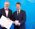 Bild: Bayerisches Innenministerium / Matthias Pfützner
Innenstaatssekretär Sandro Kirchner (rechts) verleiht die Kommunale Verdienstmedaille in Silber an Michael Cerny.