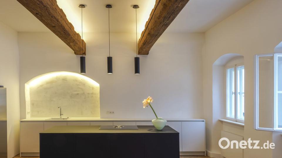 Blick in die moderne Küche, in der die historischen Deckenbalken durch die Beleuchtung in Szene gesetzt werden. Auch die zurückhaltende Möblierung lässt den Raum sehr großzügig erscheinen.