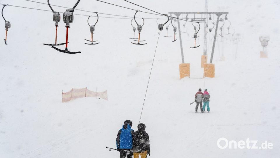 Wintersportler fahren am Predigtstuhl in St. Englmar mit einem Skilift im Schneegestöber. Bild: Armin Weigel/dpa