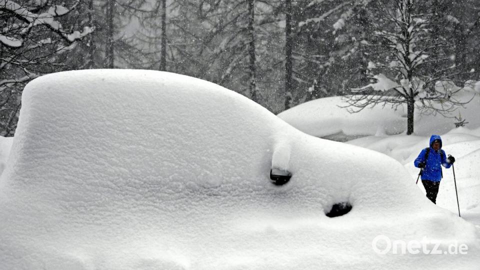 Ein Wanderer geht an einem eingeschneiten Auto im österreichischen Ramsau vorbei. Bild: Harald Schneider/APA/dpa