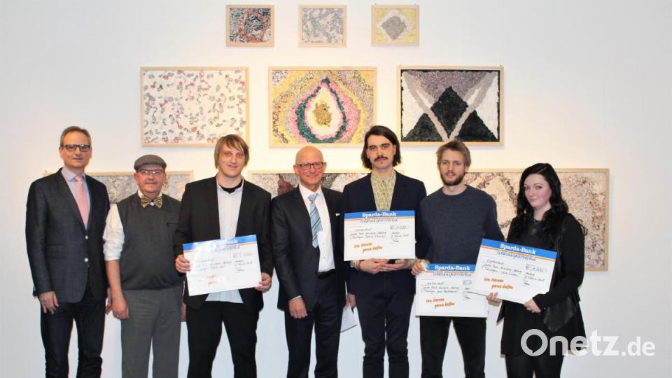 Kulturreferent Wolfgang Dersch, Bürgermeister Martin Preuß, Hauptgewinner Florian Nörl, Vorstandsvorsitzender der Sparda-Bank Georg Thurner, Patrick Ostrowsky, Jonas Beutlhauser und Lena Schabus positionieren sich vor der weltweit neuesten Erfindung des Textilsteins in Form von Gemälden. Bild: Dagmar Williamson