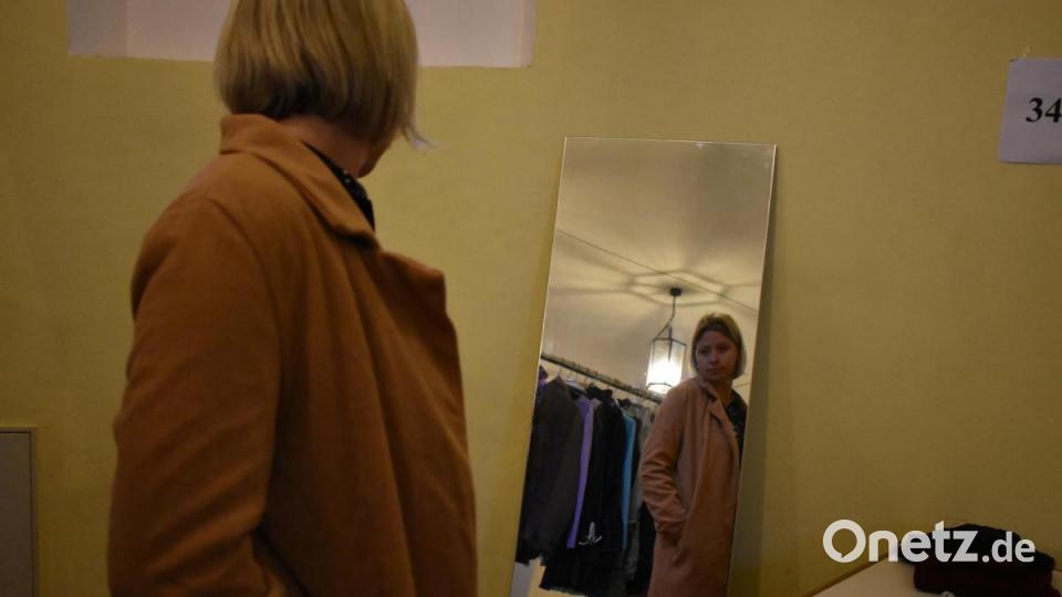 Eine junge Frau probiert einen Mantel an und betrachtet sich im Spiegel. Bild: lue