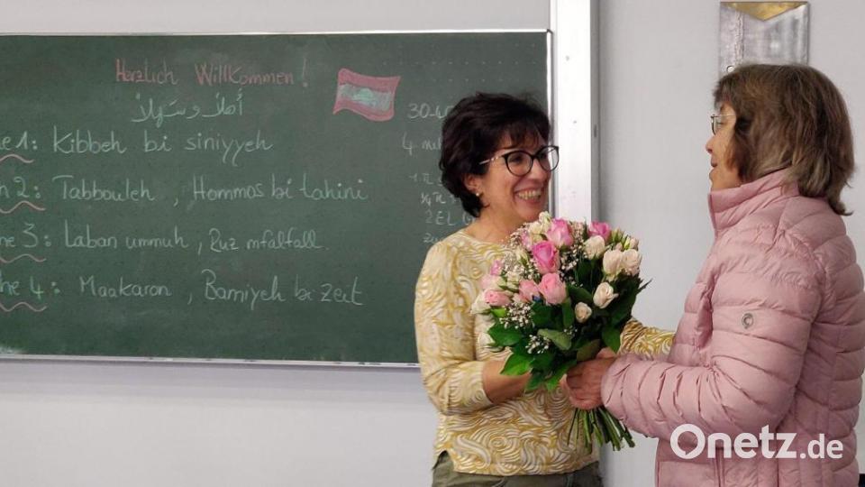 Mit einem Blumenstrauß bedankte sich Barbara Genzken-Schindler (rechts) als Geschäftsführerin der VHS Schwandorf bei Dina Bayoud-Kohl. Sie ist seit 25 Jahren Teil des Lehrpersonals der Volkshochschule und hat sich als Kochbuchautorin und Leiterin von arabischen Kochkursen weit über Schwandorf hinaus einen Namen gemacht. Auf der Tafel dahinter stehen die fremdländischen Namen der aktuellen Gerichte, denn die Gratulation erfolgte mitten in einem Kochkurs. Bild: Dobler