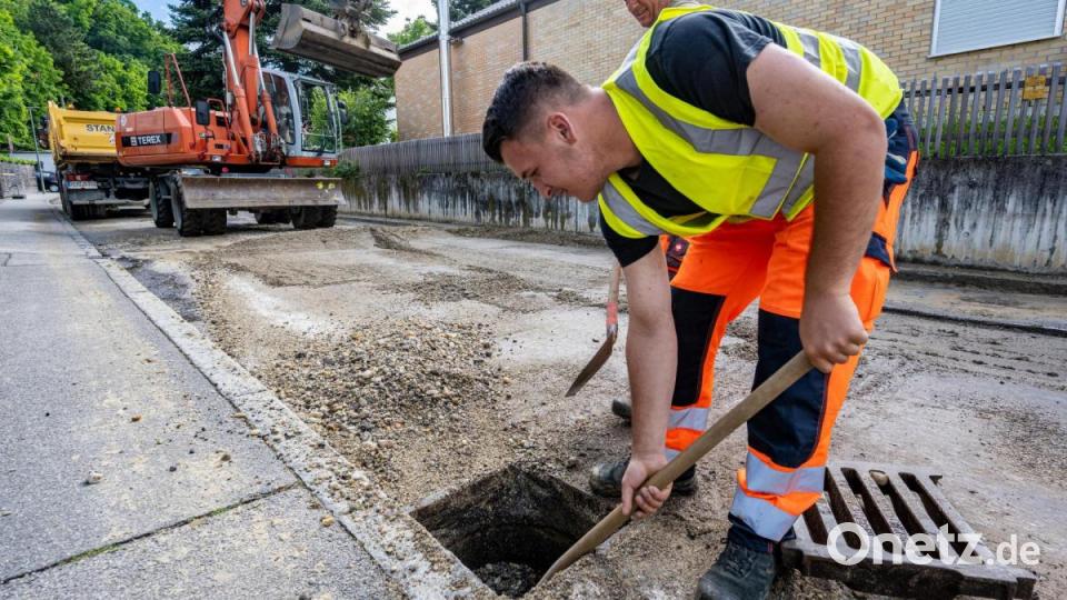 Ein Arbeiter beseitigt Kies aus einem Wasserablauf in Landshut. Bild: Armin Weigel/dpa
